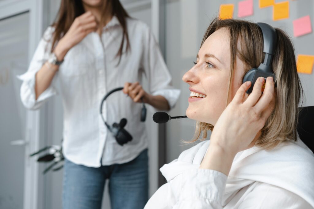 Photo by Mikhail Nilov: https://www.pexels.com/photo/close-up-photo-of-smiling-woman-wearing-headphones-7681572/ A woman smiling, using an over-ear headset to listen to someone over the phone.