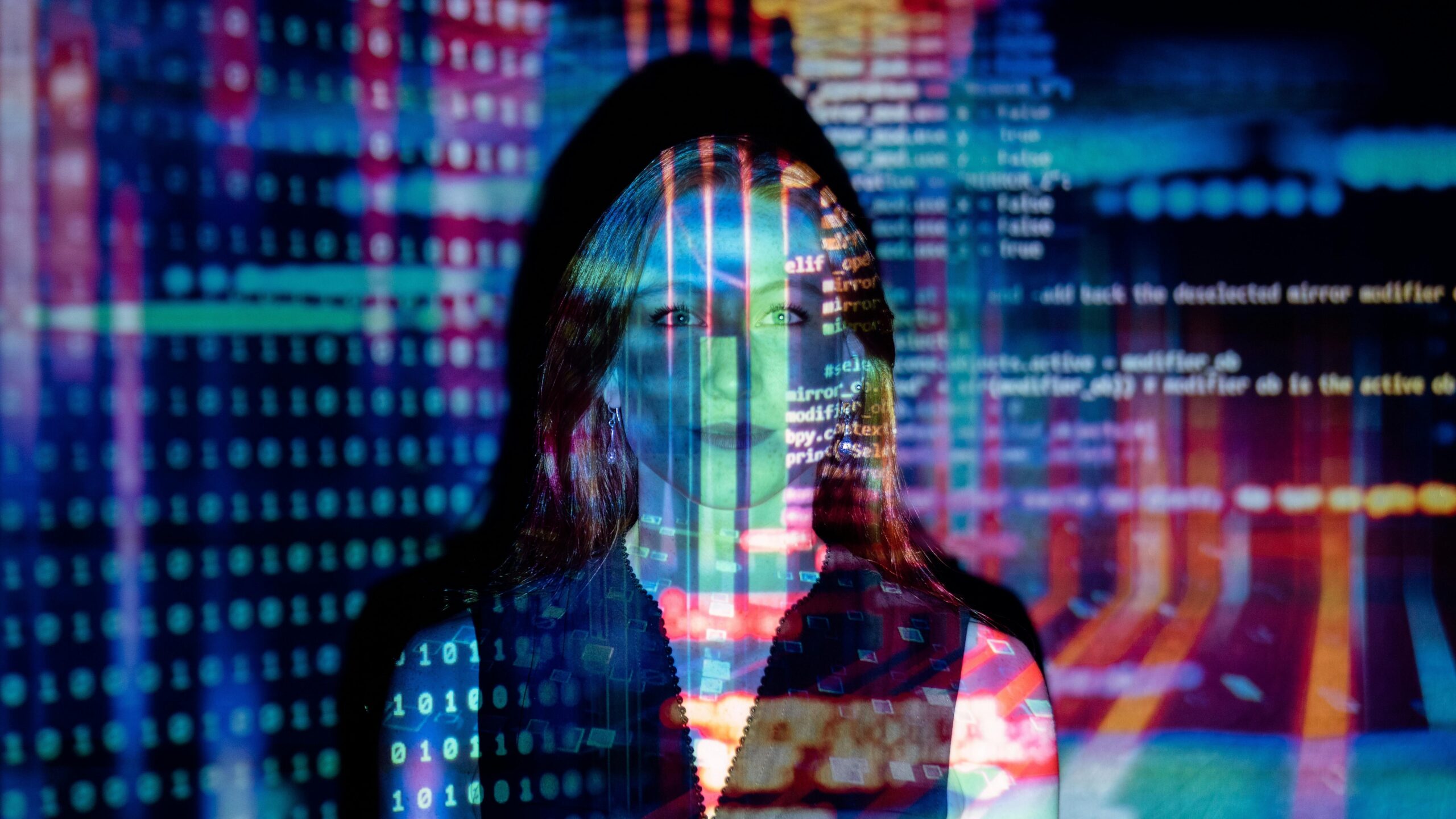 Photo by ThisIsEngineering: https://www.pexels.com/photo/code-projected-over-woman-3861969/ A woman stood with projections of website code over her face.